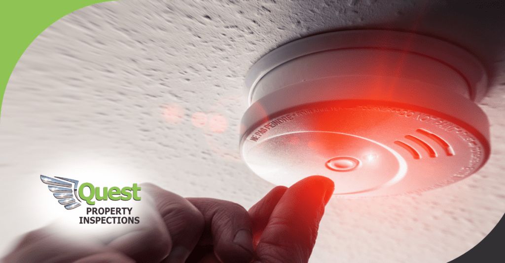 Finger pressing red-lit ceiling smoke alarm